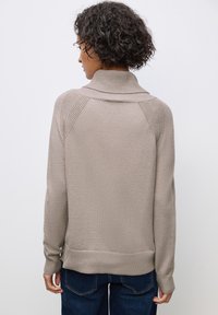 Beige tröja med en strukturerad krage och raglanärmar. Stickat material, lös passform, ribbad mudd och fåll. Bärs över mörka jeans.