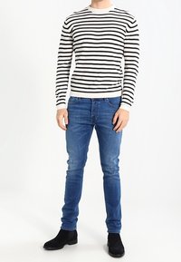 Randig tröja i beige och svart, figurnära design. Bärs med blå jeans och svarta ankelstövlar. Slät textur, standard rund hals.