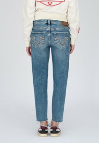 Jasnoniebieskie dżinsy o prostym kroju, z ozdobnymi tylnymi kieszeniami i surowym brzegiem. Noszone z czarno-białymi sneakersami.