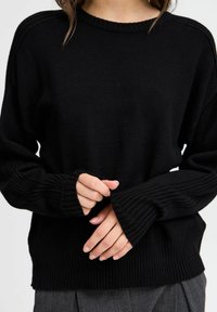 Schwarzer Strickpullover mit gerippten Bündchen und Saum, Rundhalsausschnitt und lockerer Passform. Die Textur scheint weich und leicht strukturiert zu sein.