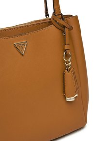 Sac à main synthétique marron avec quincaillerie dorée, un logo en forme de triangle et une étiquette amovible. Doté d'une texture lisse et d'une forme structurée.