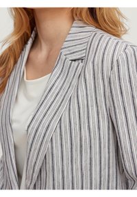 Blazer a rayas que presenta delgadas líneas verticales en navy y blanco. Los materiales parecen ligeros con un diseño estructurado de cuello y solapa.