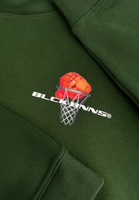 Donkergroene sweatshirt met een gedrukt grafisch ontwerp van een basketbal en een hand, met een witte net en de tekst "BLCKBNNS" eronder.