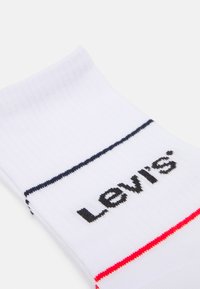 Calze di cotone bianche con texture a coste, caratterizzate da strisce orizzontali blu e rosse. Logo "Levi's" nero stampato in modo prominente.