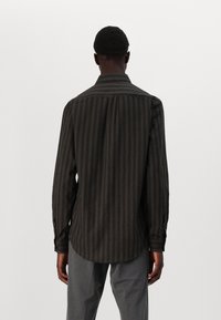 Dark striped shirt with long sleeves and a buttoned collar, featuring a smooth texture and a curved hem. Worn with gray pants.