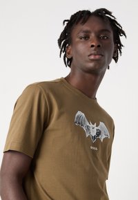 Brown cotton t-shirt featuring a graphic of a bat in flight. Crew neckline, short sleeves, and 'BOSS' text beneath the graphic.