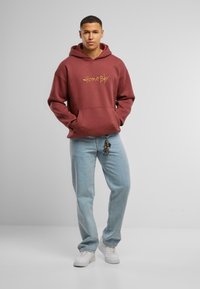 Bordový mikina s prednou vačkou a žltým nápisom "Home Boy". V kombinácii s svetlomodrými džínsami a bielymi teniskami.