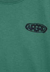 Zelená látka s malým čiernym oválnym logom na hornej časti hrudníka s nápisom „AIRGRID“ v tučných, štýlovo upravených písmach.