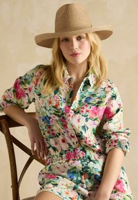 Cămașă și pantaloni scurți cu model floral, dintr-un material ușor, în nuanțe de roz, albastru și verde. Asortate cu o pălărie de paie cu boruri largi.