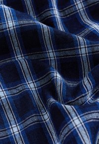 Tissu à carreaux bleu marine avec des lignes contrastantes blanches et bleu clair, présentant un tissage texturé et un drapé doux.