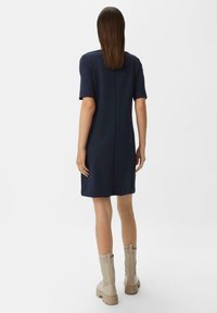 Marineblaues Kurzarmkleid mit geradem Schnitt und einer Rückennaht. Kombiniert mit cremefarbenen Stiefeln bis zur Mitte der Wade, hergestellt aus strukturiertem Material.
