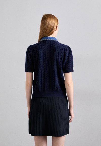 Navy knitted sweater with cable pattern, short puff sleeves, and a denim collar, paired with a black ribbed skirt.
