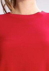 Blouse rouge avec une texture lisse et un col rond simple, dotée de manches courtes et d'un design de corsage ajusté.