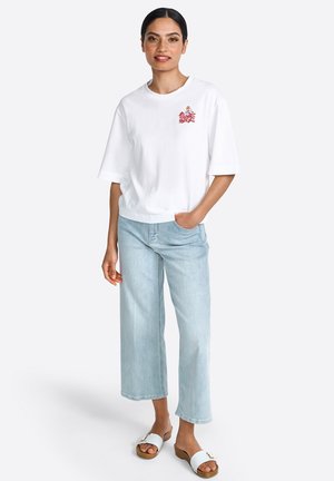 Weißes Baumwoll-T-Shirt mit kurzen Ärmeln, das ein gesticktes Design aufweist. Kombiniert mit hellblauen weiten Jeans und Sandalen mit Holzabsatz.