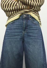 Džínsy z denimu v stredne modrej farbe s voľným strihom. Obsahujú päť vreciek, zapínanie na gombíky a jemné vyblednutie na materiáli.