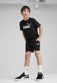T-shirt noire Puma avec logo, shorts noirs, baskets noir et blanc, chaussettes blanches avec logo. Design athlétique simple, en coton, coupe décontractée.