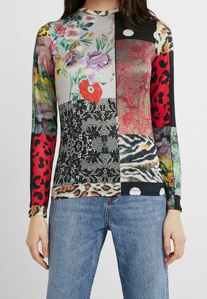 Top de manga larga ajustado con parches que combinan patrones florales, animales y abstractos en colores vibrantes, acompañado de pantalones vaqueros azules.