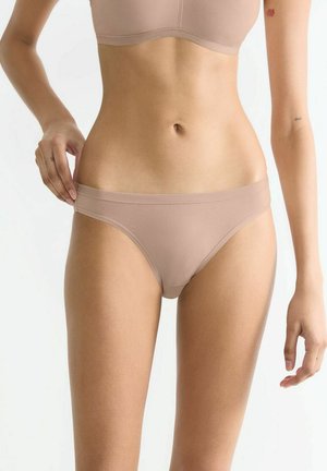 Nude ribbed fabric thong with a smooth waistband, featuring a minimalist design and seamless edges for comfort and a discreet appearance.