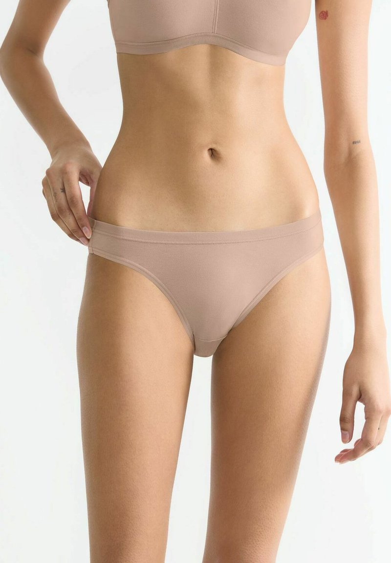 Nudefarbener, gerippter Stofftanga mit glattem Bund, der ein minimalistisches Design und nahtlose Kanten für Komfort und ein dezentes Erscheinungsbild bietet.