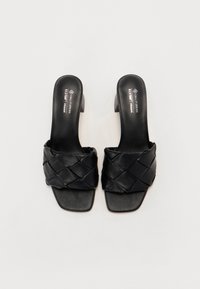 Black vegan leather slide sandals with a woven upper, square toe, and a low block heel. Smooth texture and minimal branding.