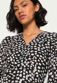 Vestido preto com um padrão de pinceladas brancas, apresentando um decote em V, mangas bufantes e um tecido suave para uma aparência texturizada.