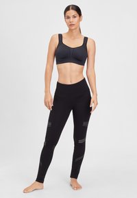 Sort sports-bh med brede stropper, formede skåle og sømløst design. Sorte tights med høj talje og reflekterende stribe accenter.