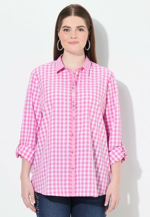 Rosa-weiße Karobluse mit durchgehender Knopfleiste, aufgerollten Ärmeln und dekorativen Nähten. Weicher Stoff und lässiger Schnitt.