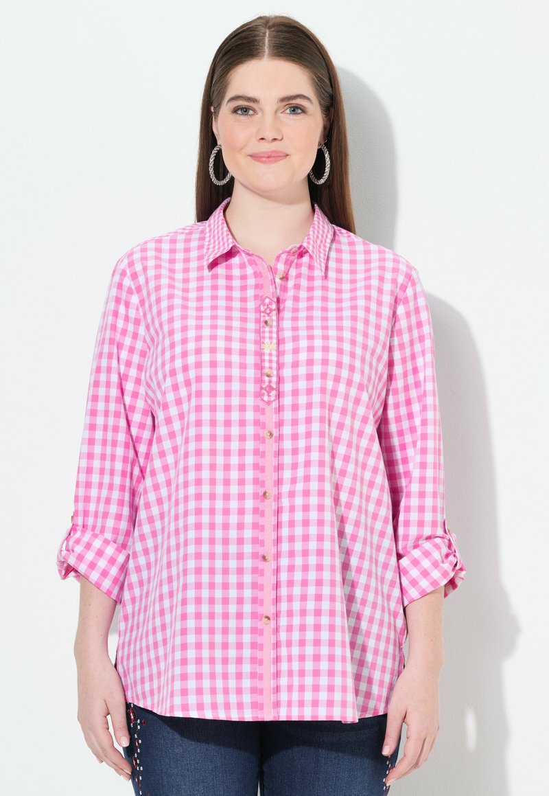 Rosa-weiße Karobluse mit durchgehender Knopfleiste, aufgerollten Ärmeln und dekorativen Nähten. Weicher Stoff und lässiger Schnitt.