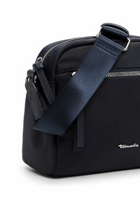 Navy nylon crossbody bag with a smooth texture, silver zipper, adjustable strap, and embossed brand logo on the lower right corner.