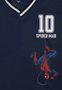 Marineblå jersey-T-skjorte med v-hals, hvit stripete kant, nummer 10, teksten "SPIDER-MAN" og en illustrasjon av Spider-Man som henger ned.