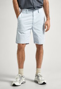 Pantaloni corti azzurri chiari con taglio dritto, realizzati in cotone, dotati di passanti per cintura e tasche laterali. Abbinati a sneakers bianche e grigie.