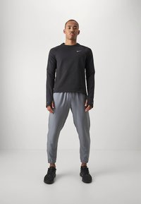 Camisola atlética preta de mangas compridas com decote redondo, combinada com calças de treino cinza claro afuniladas. Ténis atléticos pretos completam o conjunto.