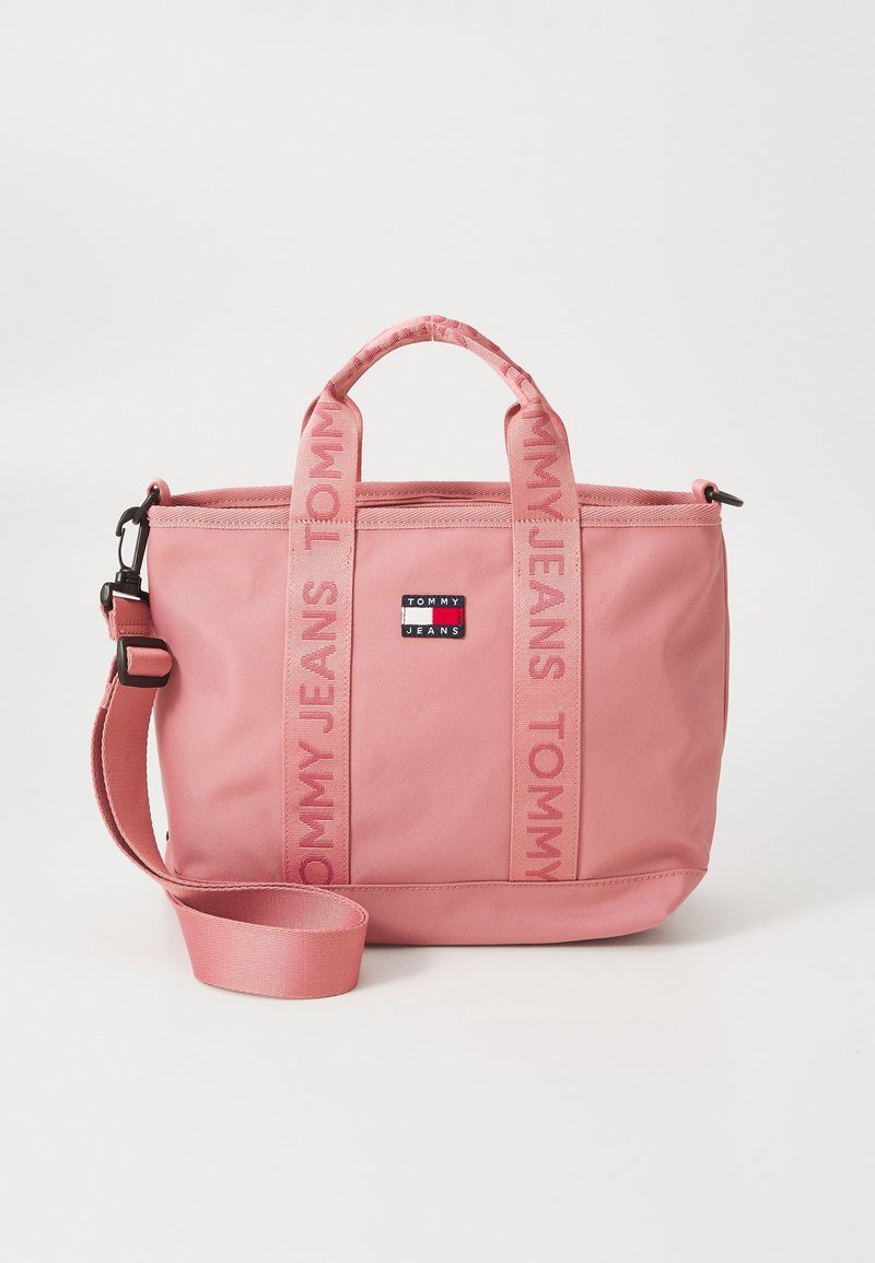Sac tote rose Tommy Jeans avec doubles poignées, bandoulière ajustable et patch logo à l'avant sur fond uni.