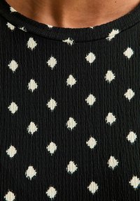 Zwarte gestructureerde stof met witte ruitvormige stippen. Eenvoudige ronde halslijn, medium geribbelde oppervlakte. Patroon gelijkmatig verdeeld.