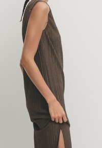 Ruskean raidoitettu hihaton paita rentoa leikkausta, jossa on sivureikä. Tekstuurin näyttää olevan pehmeä ja rakenteellinen, mikä parantaa vaatteen virtaavuutta.