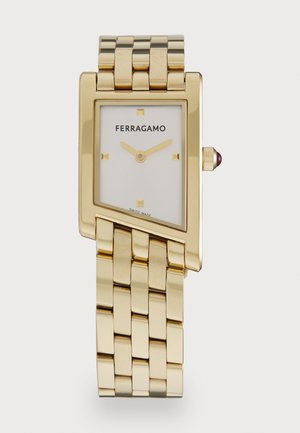 Goldenes rechteckiges Armband mit einem weißen Zifferblatt, goldenen Stundenmarkierungen und einem strukturierten Metallarmband. Die Krone hat einen kleinen roten Akzent.