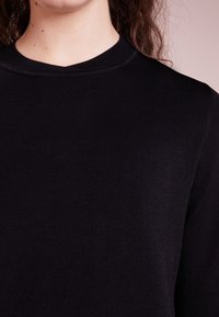 Maglione nero lavorato a maglia con scollo rotondo, tessuto testurizzato e un aspetto liscio e morbido. Dettaglio su maniche e colletto.
