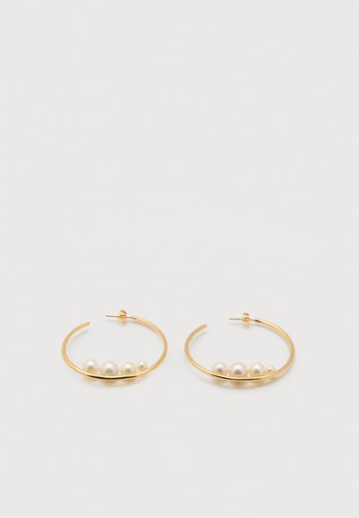 Χρυσά σκουλαρίκια κρίκοι, καθένα διακοσμημένο με τέσσερις λευκές πέρλες διαφορετικών μεγεθών σε λευκό φόντο.
