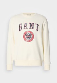 Kremowy sweatshirt z długimi rękawami, okrągłym dekoltem i zniszczoną grafiką logo GANT w kolorze czerwonym i niebieskim. Miękki materiał.