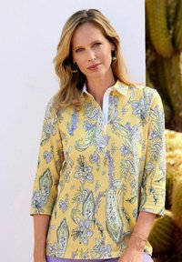 Geel pullover met een bloemen-paisleypatroon in paars en groen, met een kraag en een witte sluiting, en driekwart mouwen.