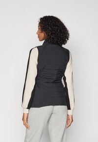 Čierna prešívaná bunda s vysokým golierom, rukávmi v krémovej farbe s farebnými blokmi a s úzkym pásom. Hladká textúra s prešívaným vzorom na zadnej strane.