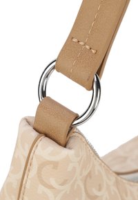 Tan syntetisk skulderrem med syede detaljer, der er fastgjort via en sølvmetallring til en beige taske med mønstret tekstur.