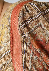 Tissu à motifs marron et or avec des accents en dentelle corail. Comprend des designs paisley et géométriques complexes avec des détails rayés.