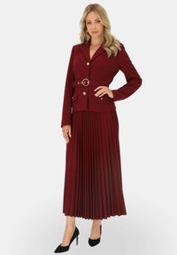 Bordowy żakiet z paskiem i dwiema przednimi kieszeniami, zestawiony z plisowaną bordową spódnicą. Strój ma dopasowany krój i gładką teksturę.