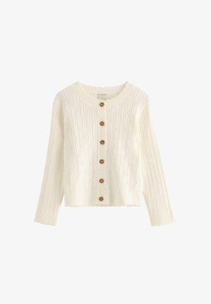 White knitted cardigan with a ribbed texture, scalloped edges, and brown buttons down the front. Long sleeves with a round neckline.