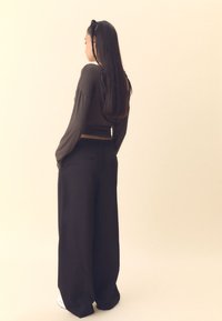 Czarne spodnie o szerokich nogawkach oraz ciemnobrązowa bluzka z długim rękawem, charakteryzujące się dopasowanym krojem, miękkimi teksturami i swobodną sylwetką.