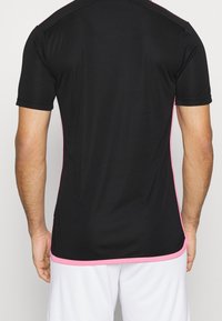 Musta urheilupaita, jossa on lyhyet hihat, vaaleanpunaiset sivukoristeet ja sileä, kevyt kangas. Yksinkertainen, istuva malli.