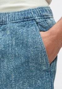 Krótkie spodenki dżinsowe w jasnoniebieskim kolorze z elastycznym pasem, wyposażone w boczne kieszenie i z efektem wyblakłego denimu, prezentujące casualowy styl.