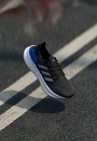 Black athletic shoe with a textured upper, features blue accents, three grey stripes, and a white midsole labeled "LIGHTBOOST."