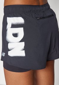 Črne atletske kratke hlače z zadrgo, ki na strani vsebujejo velik bel napis "LDN" in so narejene iz lahkega, zračnega materiala.